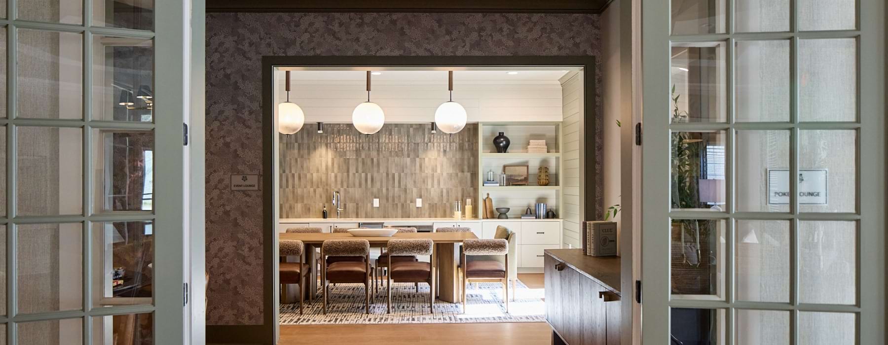 Private dining space with a large table, pendant lighting, and an open kitchen with modern finishes and built-in shelving